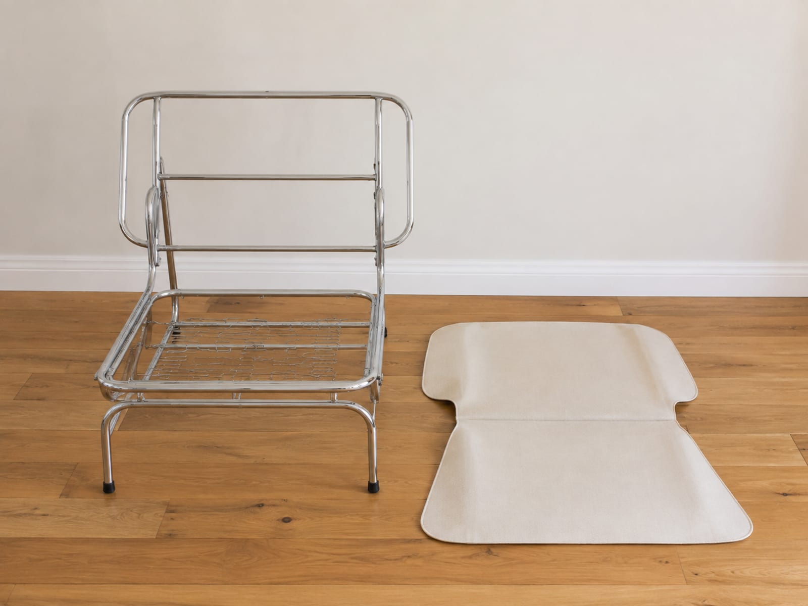 A chair cover removed and laid flat on floorboards beside the bare chair frame it came off, the plain chrome-plated steel structure clearly visible