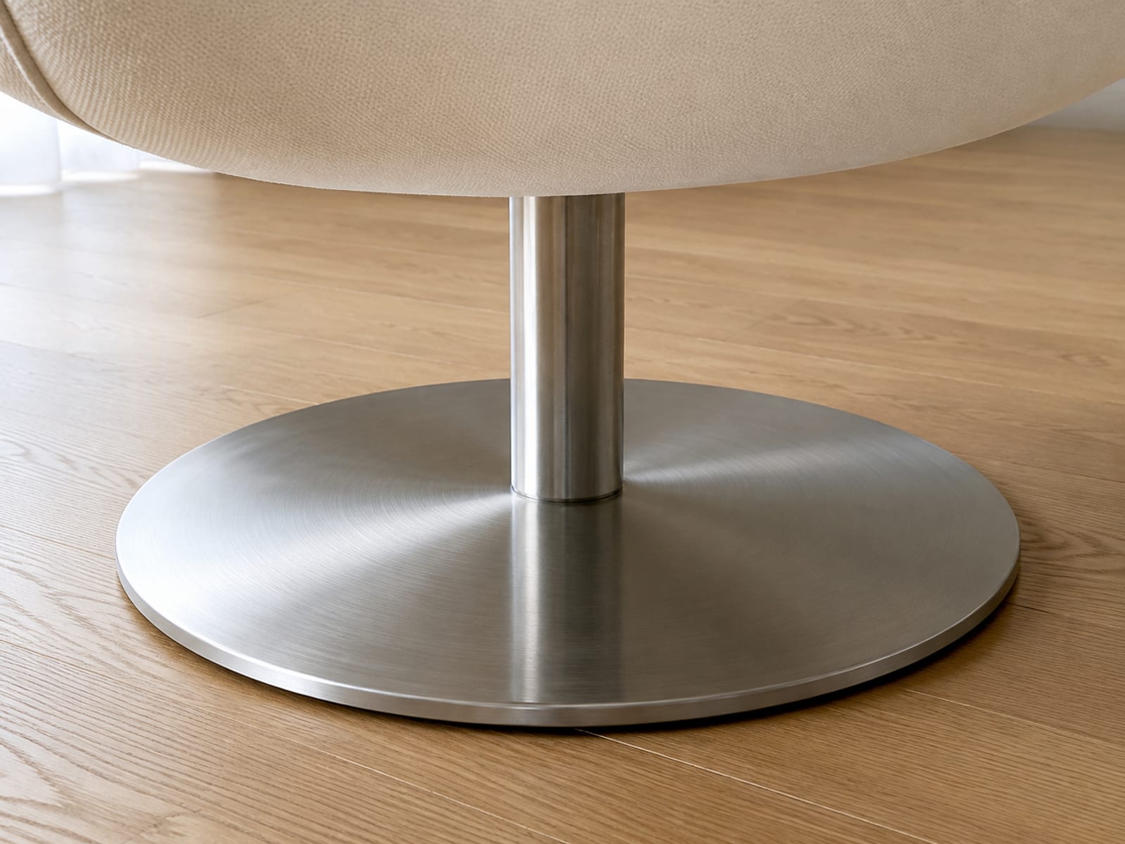 A low close view of the round steel base and central column of a swivel accent chair, framed from floor level with the underside of the seat above