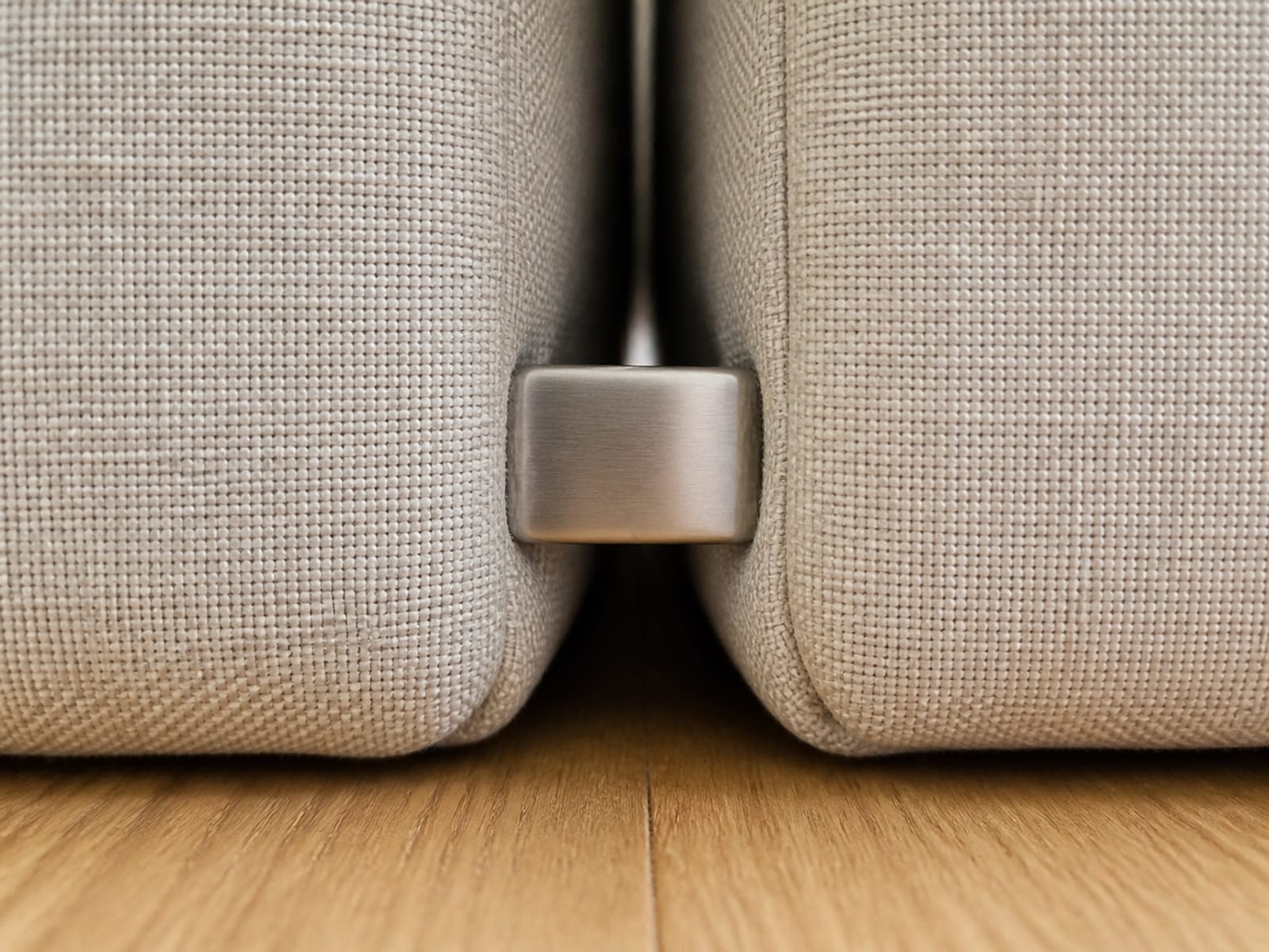 An extremely close low view into the gap where two sectional modules meet, with a plain unmarked steel catch holding them together in the shadow between their bases