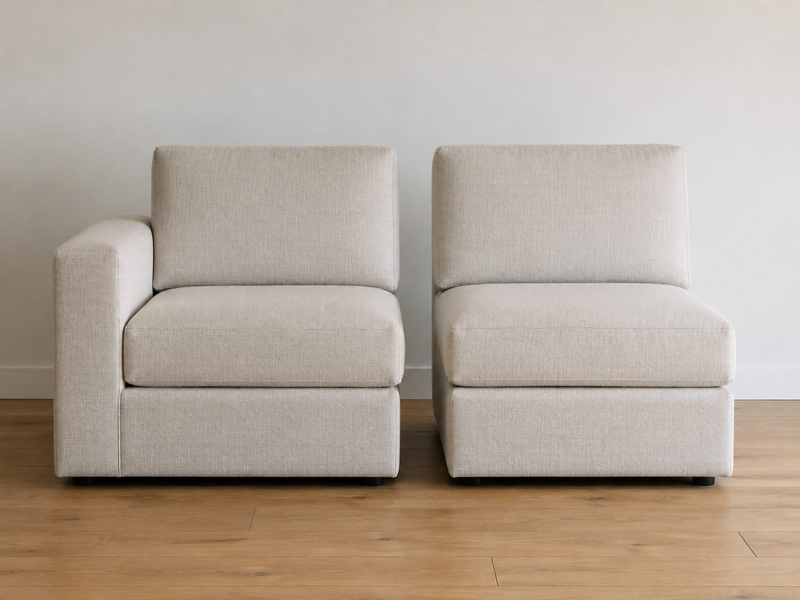 Two upholstered seat modules of identical size side by side on bare oak floorboards, the left with a single arm on its outer edge and the right completely armless