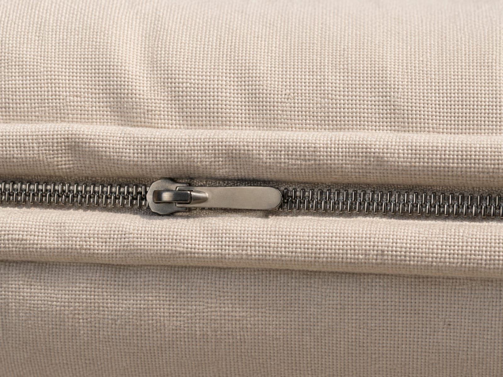 An extremely close view along a closed zip running through the base seam of a boneless seat unit, the teeth interlocked and the plain pull lying flat against the fabric
