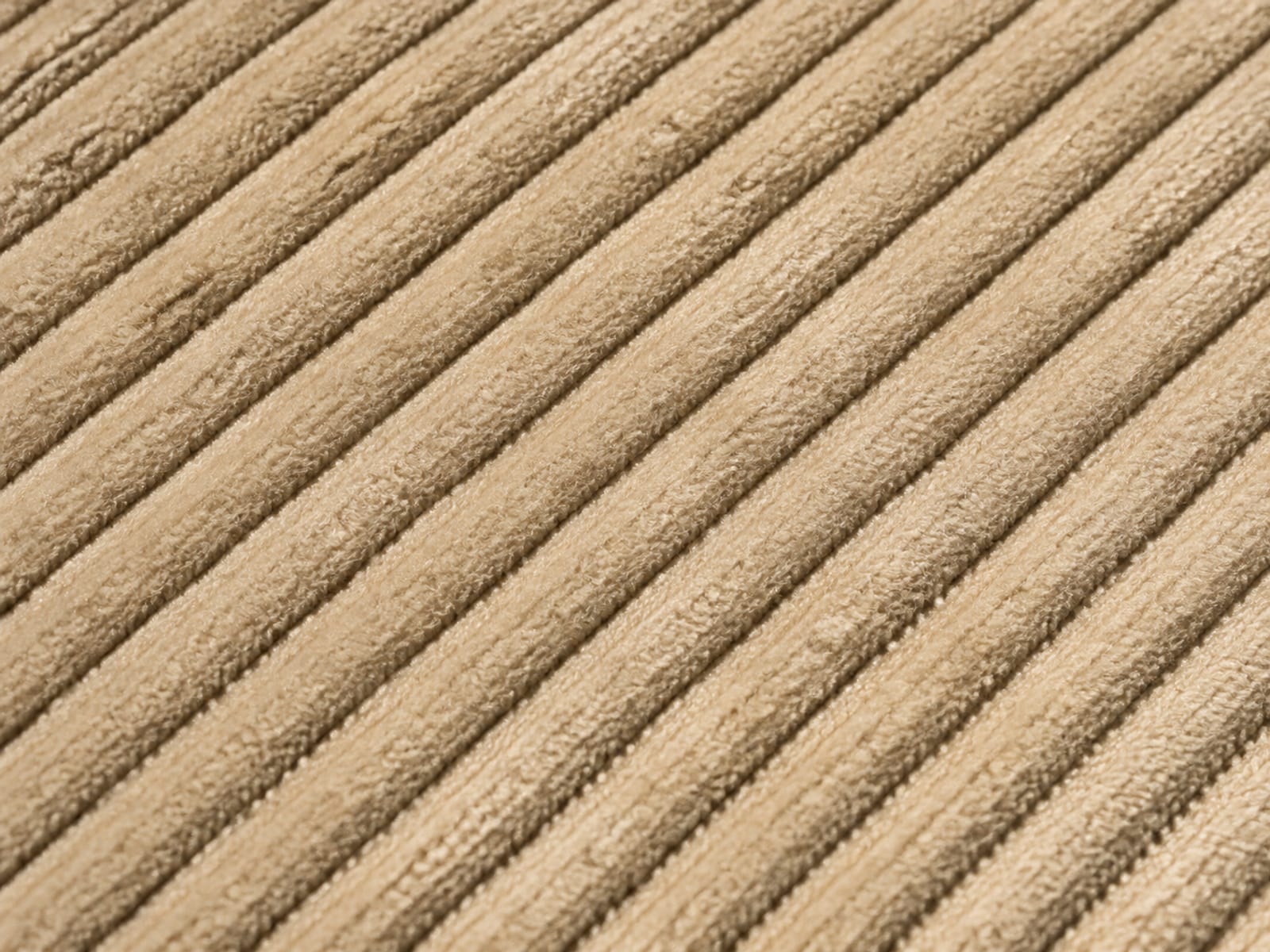 An extremely close view of ribbed corduroy upholstery filling the frame, the ribs running diagonally under a low raking light so the depth of the pile reads