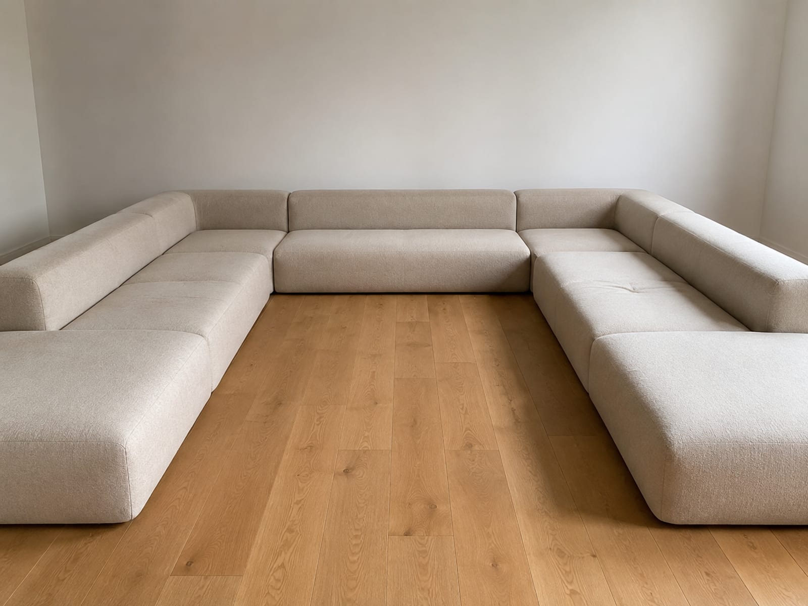 A large U-shaped boneless sectional seen from standing height at the open end, both arms running away toward the far wall with bare floor enclosed between them