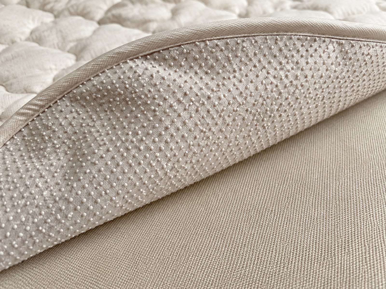 A corner of a quilted protector folded back on a sofa seat, showing the raised texture of its gripping underside