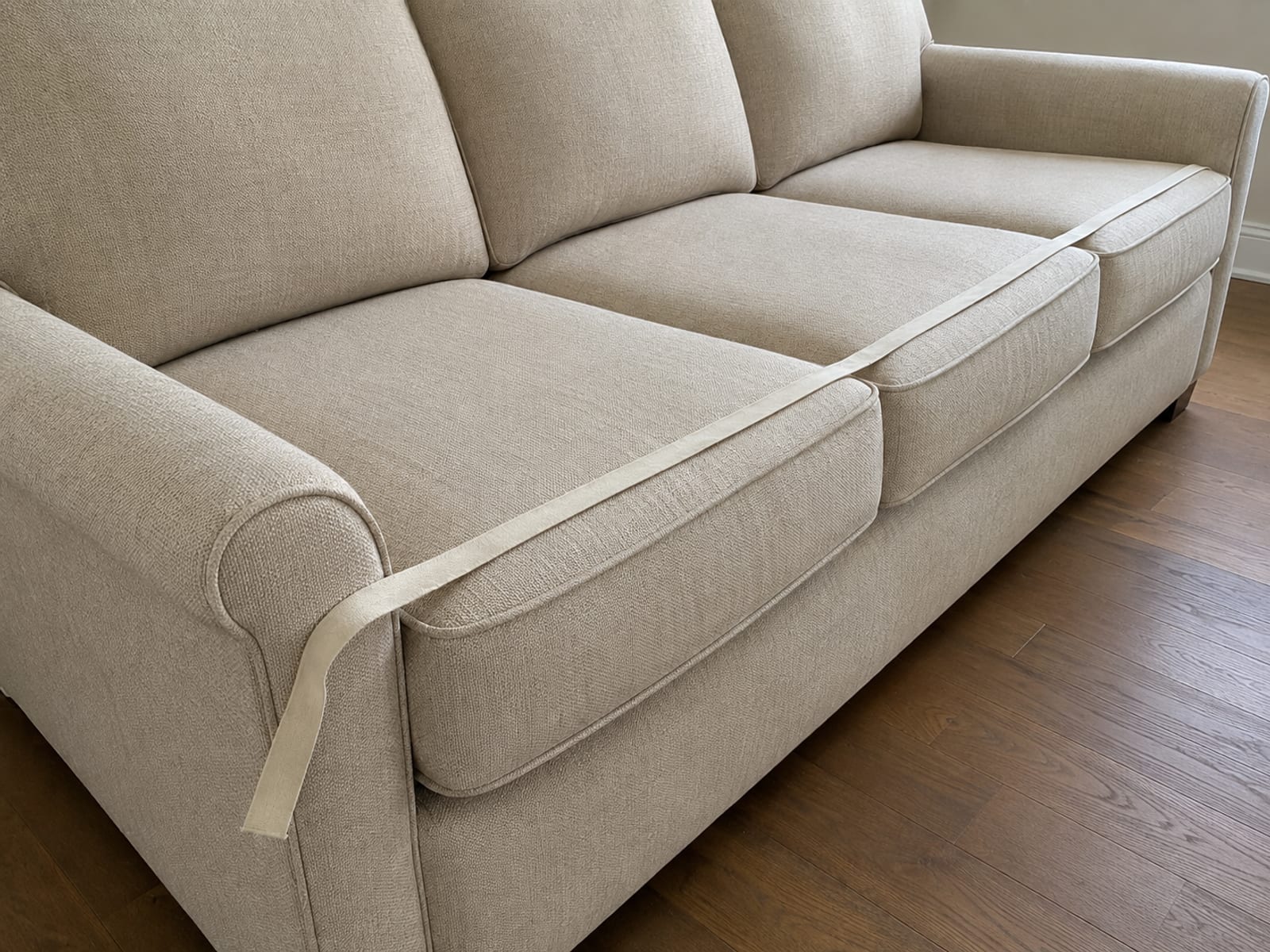 A blank cloth measuring tape lying unrolled along the front edge of a bare sofa's seat cushions