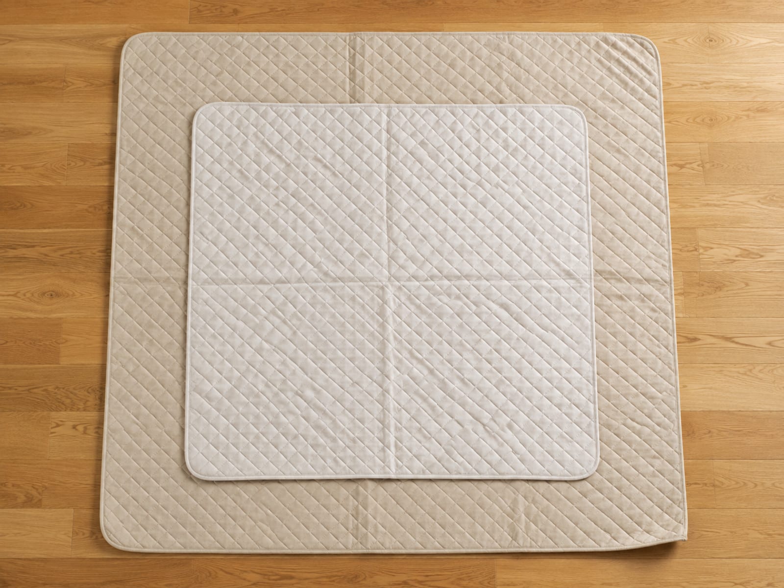 Two quilted protectors of different sizes laid flat and overlapping on bare floorboards