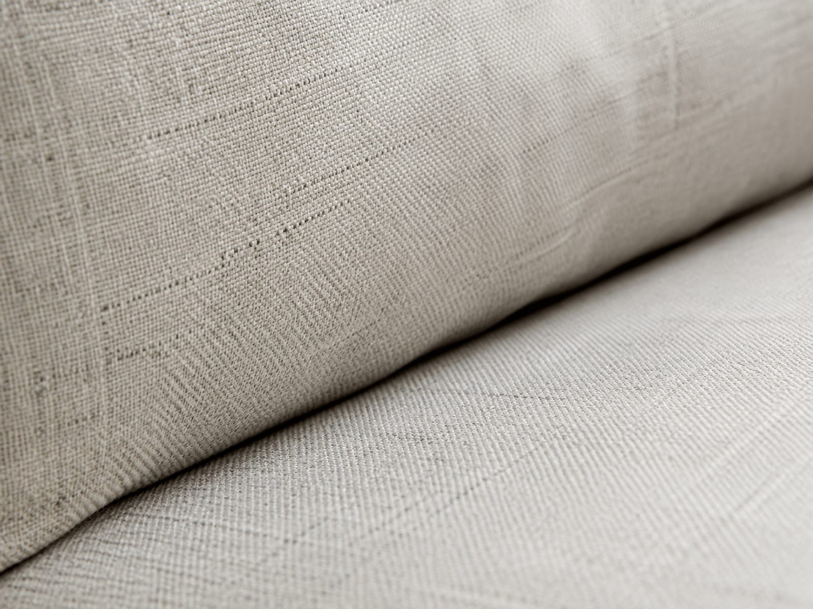 An extremely close side view of the fold where a thick upholstered back cushion meets the seat cushion, the shadowed channel between them running diagonally under raking light