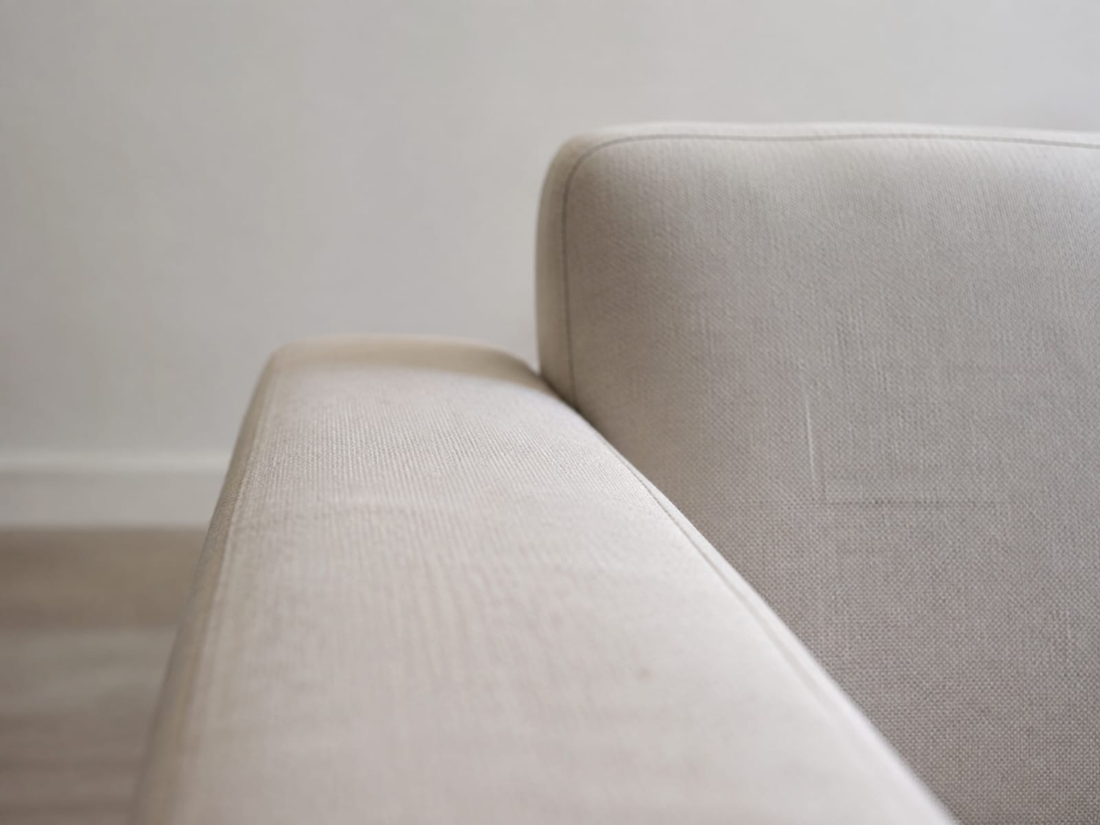 A wide panel of plain upholstery cloth thrown loosely over a bare wooden chair frame in an empty room, draping rather than fitted