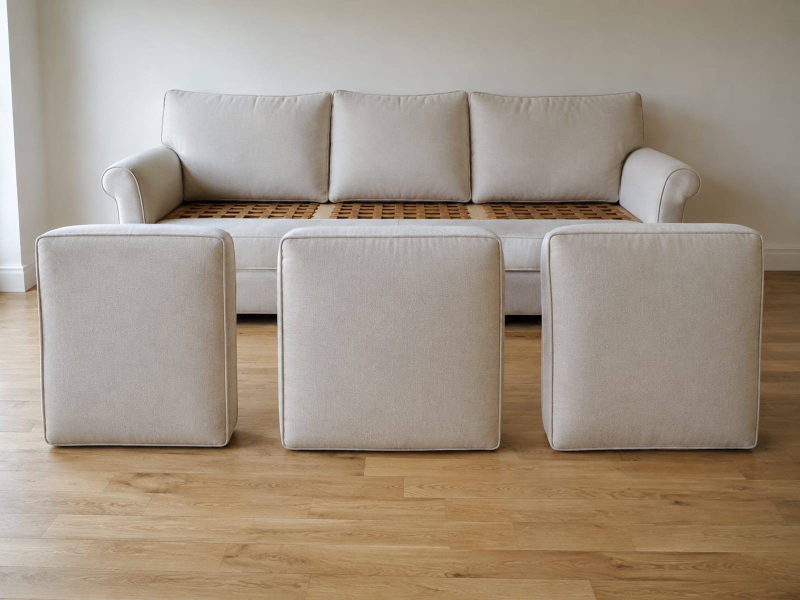 Three seat cushions removed from a sofa and stood on their long edges in a row on floorboards, the empty seat platform visible behind them