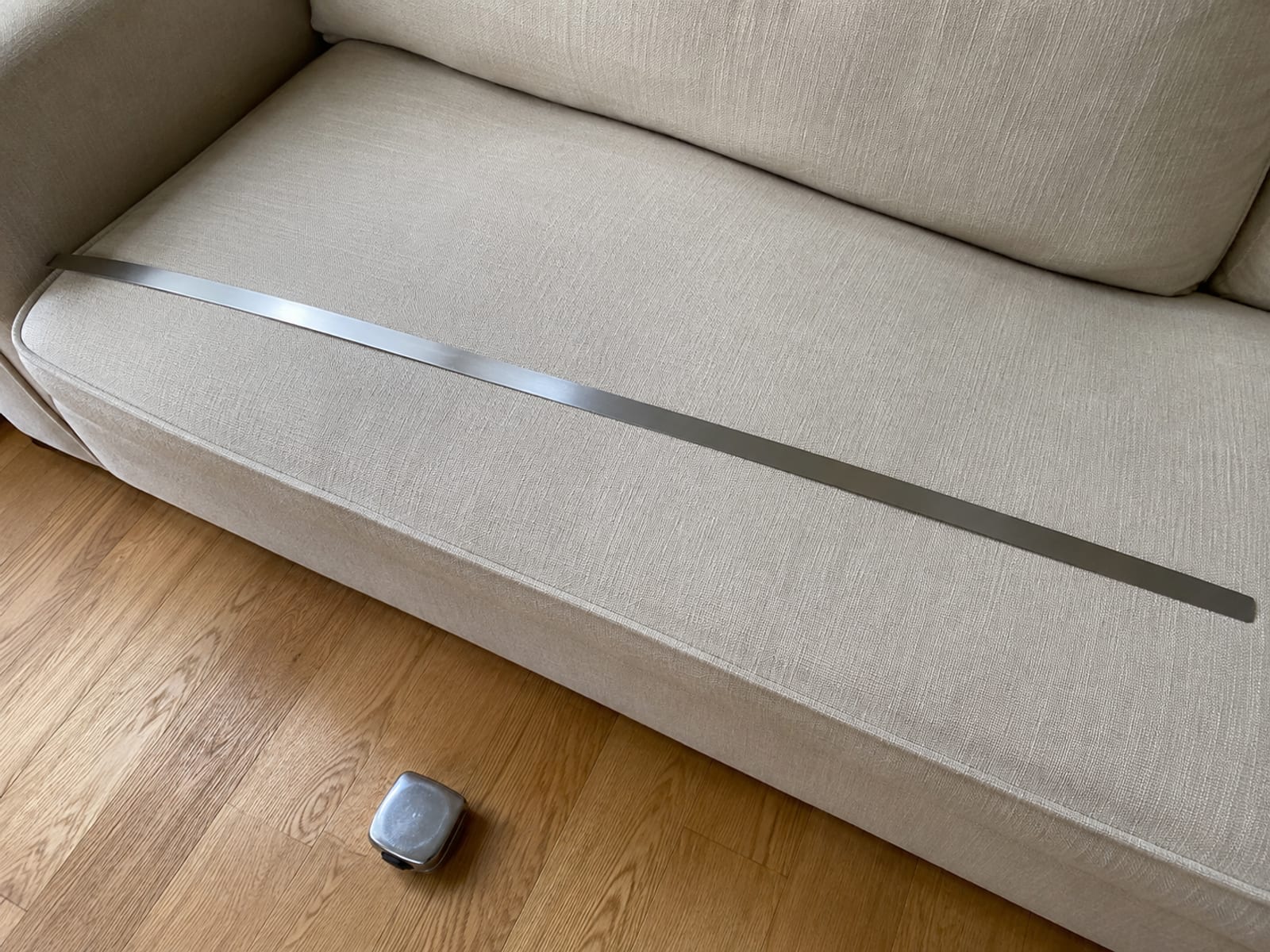 A steel tape measure extended flat across the full width of a pale woven seat cushion, its case set down on the floorboards below