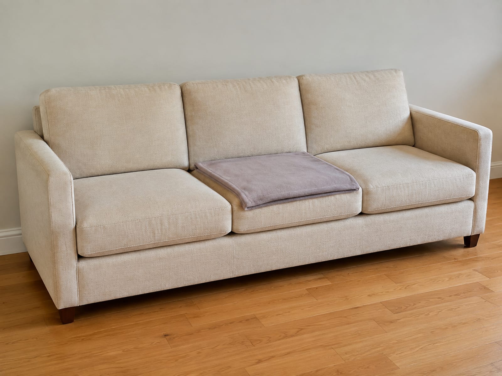 A single soft blanket folded once and laid flat over one seat cushion of an otherwise uncovered three-seat sofa