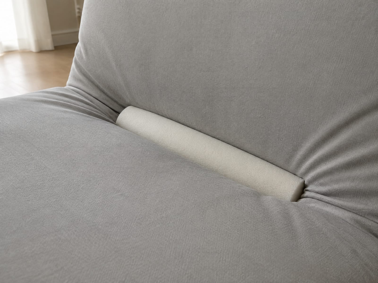 A soft cylindrical foam roll pushed into the gap between a sofa seat and back cushion, holding the fitted cover taut on either side