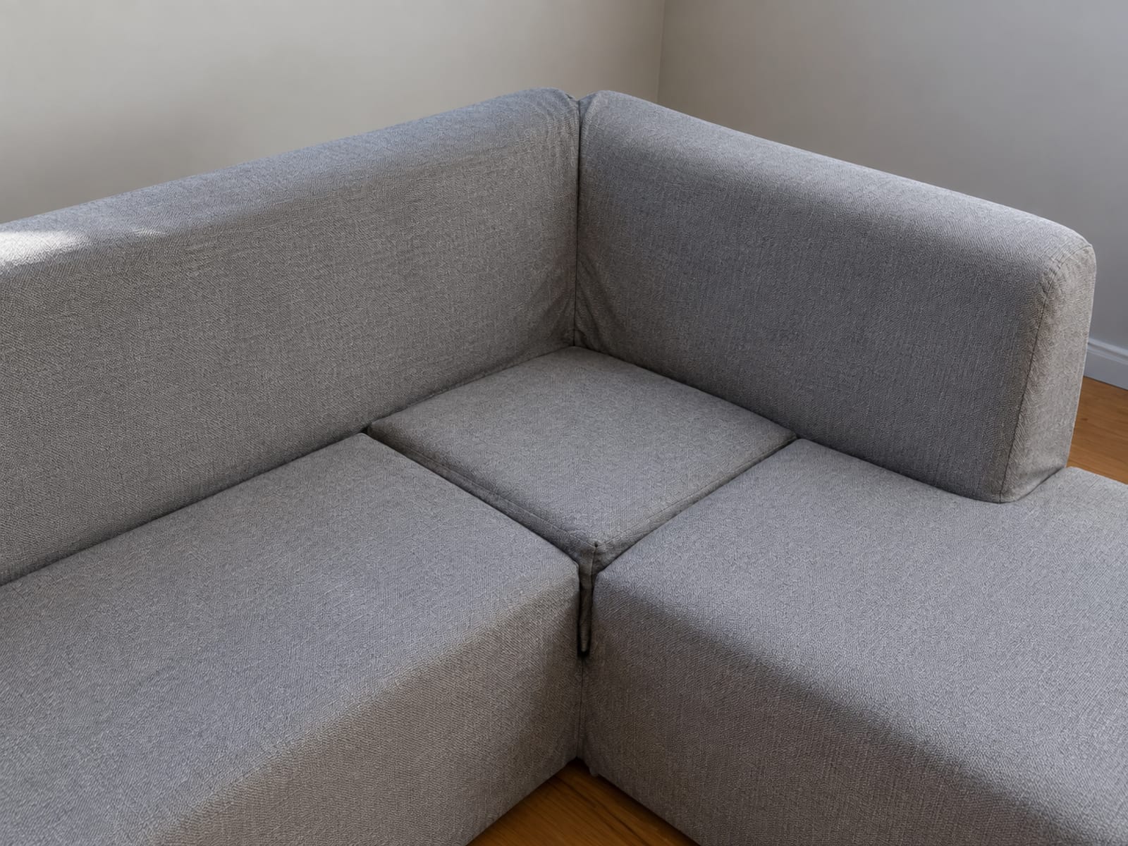 The inside corner of an L-shaped sectional with separate fitted cover pieces over each run, meeting in a visible seam at the corner
