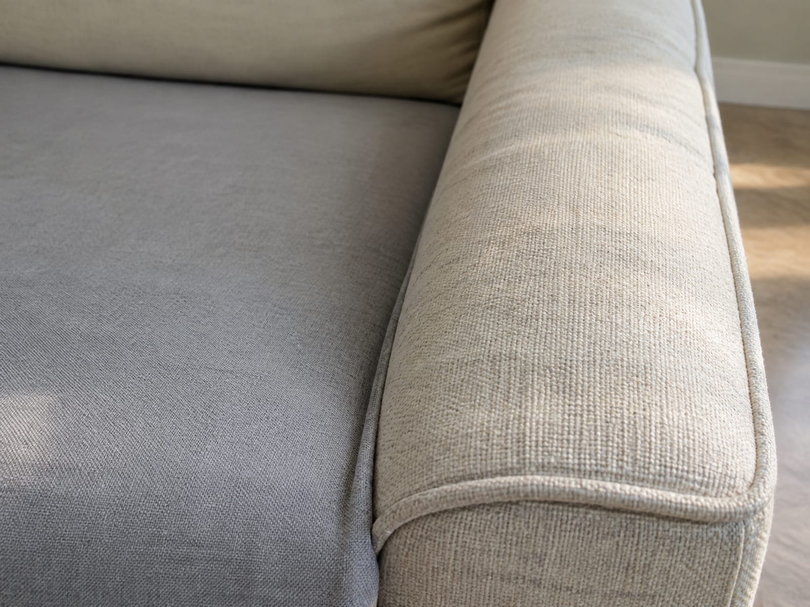 A close view along a sofa arm where the edge of a fitted seat cover stops, covered seat on one side and bare upholstery on the other