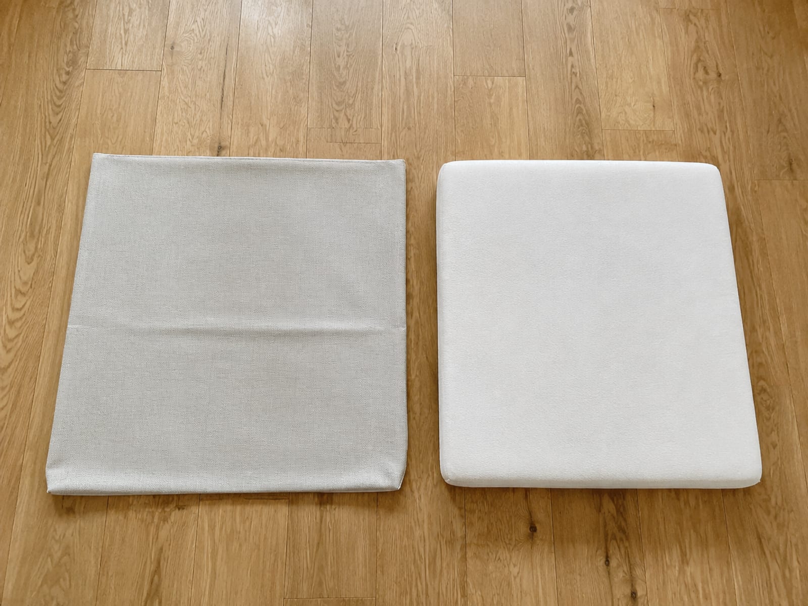 A removable upholstery cover taken off a convertible seat cushion and laid flat on bare oak floorboards beside the plain bare cushion it came from