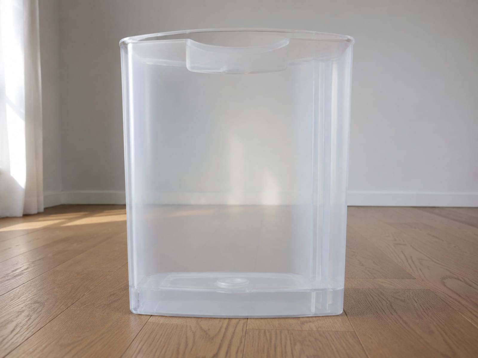 A plain translucent plastic tank, empty and dry inside, standing upright on bare floorboards in daylight