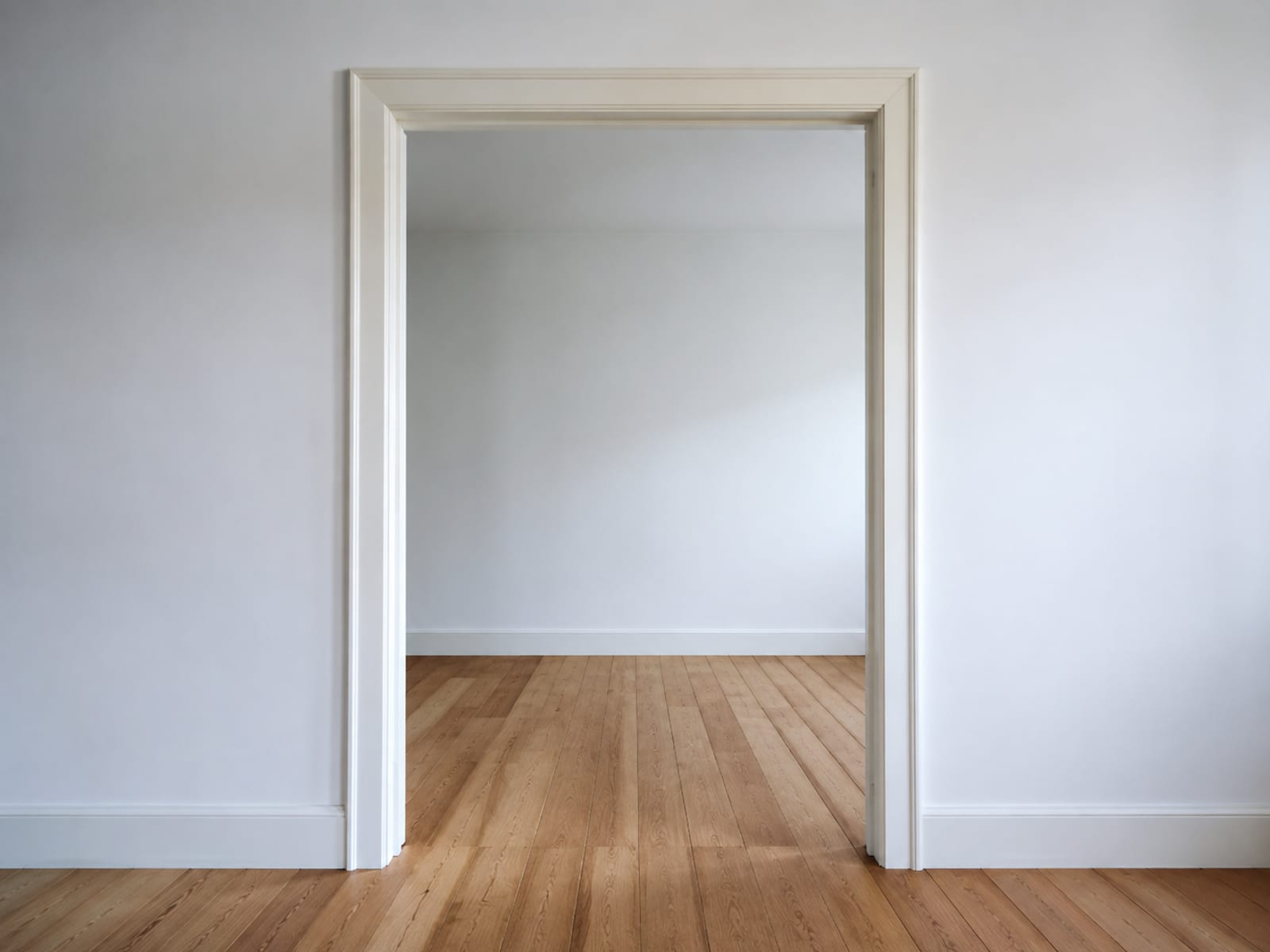 A plain empty interior door frame seen square from standing height, its two jambs and head casing forming a rectangle with bare floorboards running through into an empty room