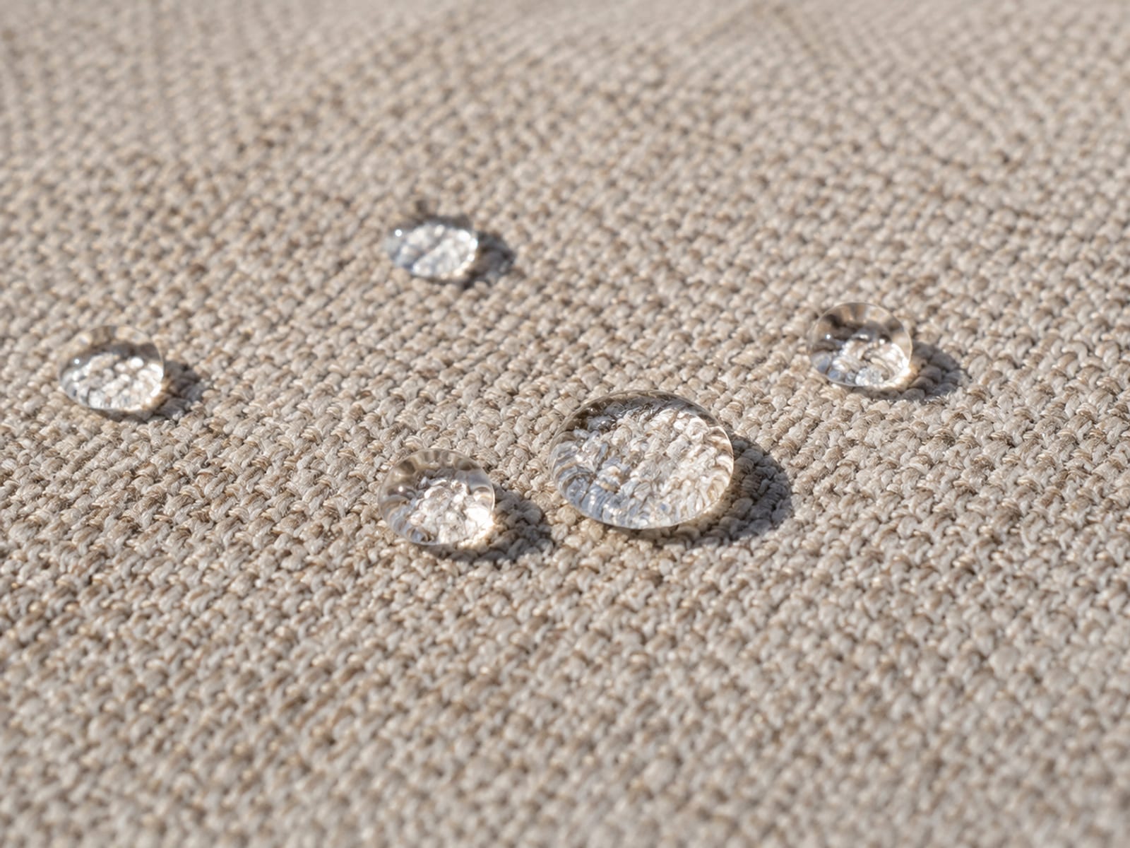 A few clean water droplets sitting beaded on a treated upholstery surface without spreading, the weave visible around them