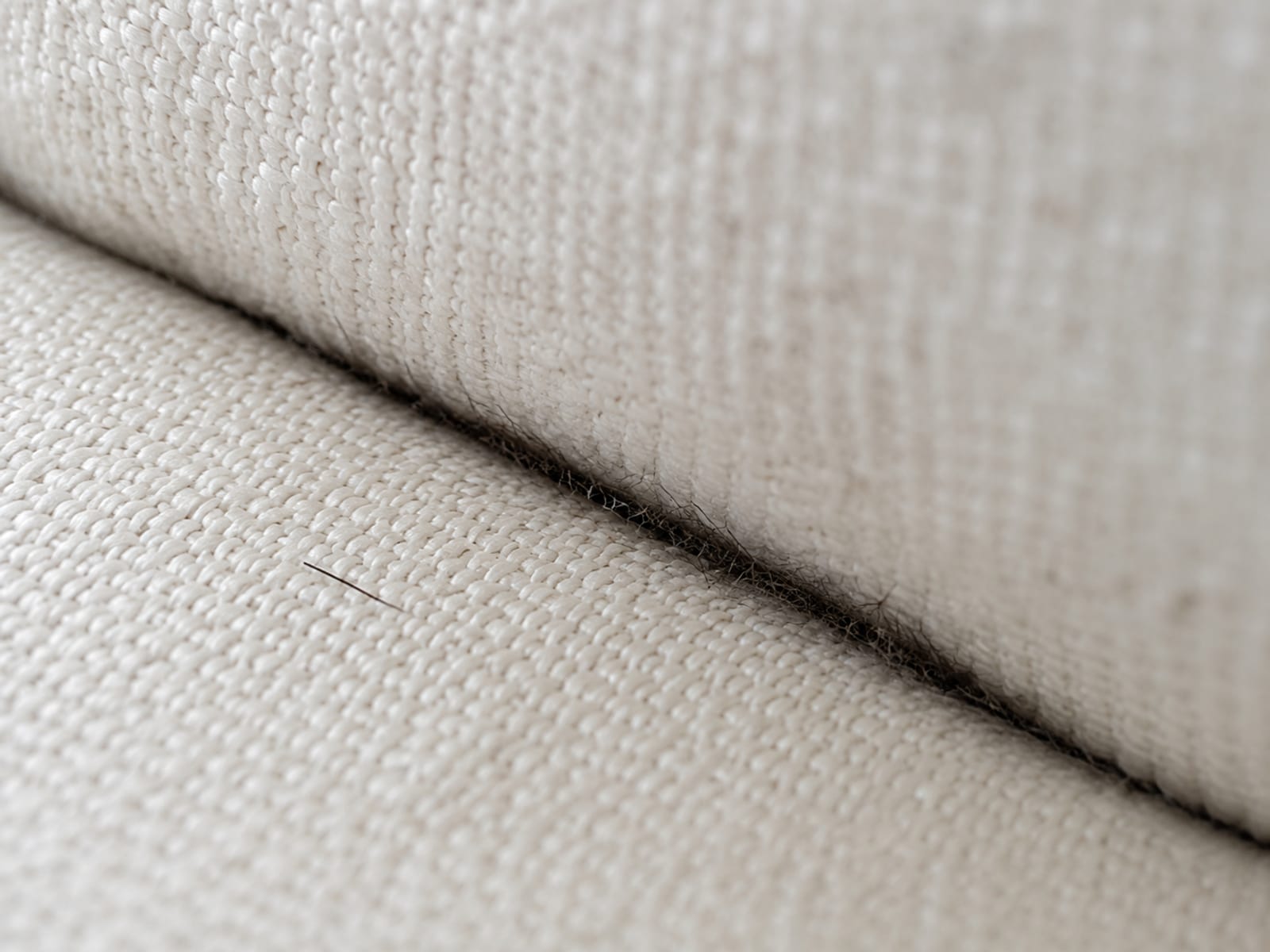 A close view along the crease where a pale woven seat cushion meets the back cushion, with short dark hair worked down into the fold between the two fabric faces