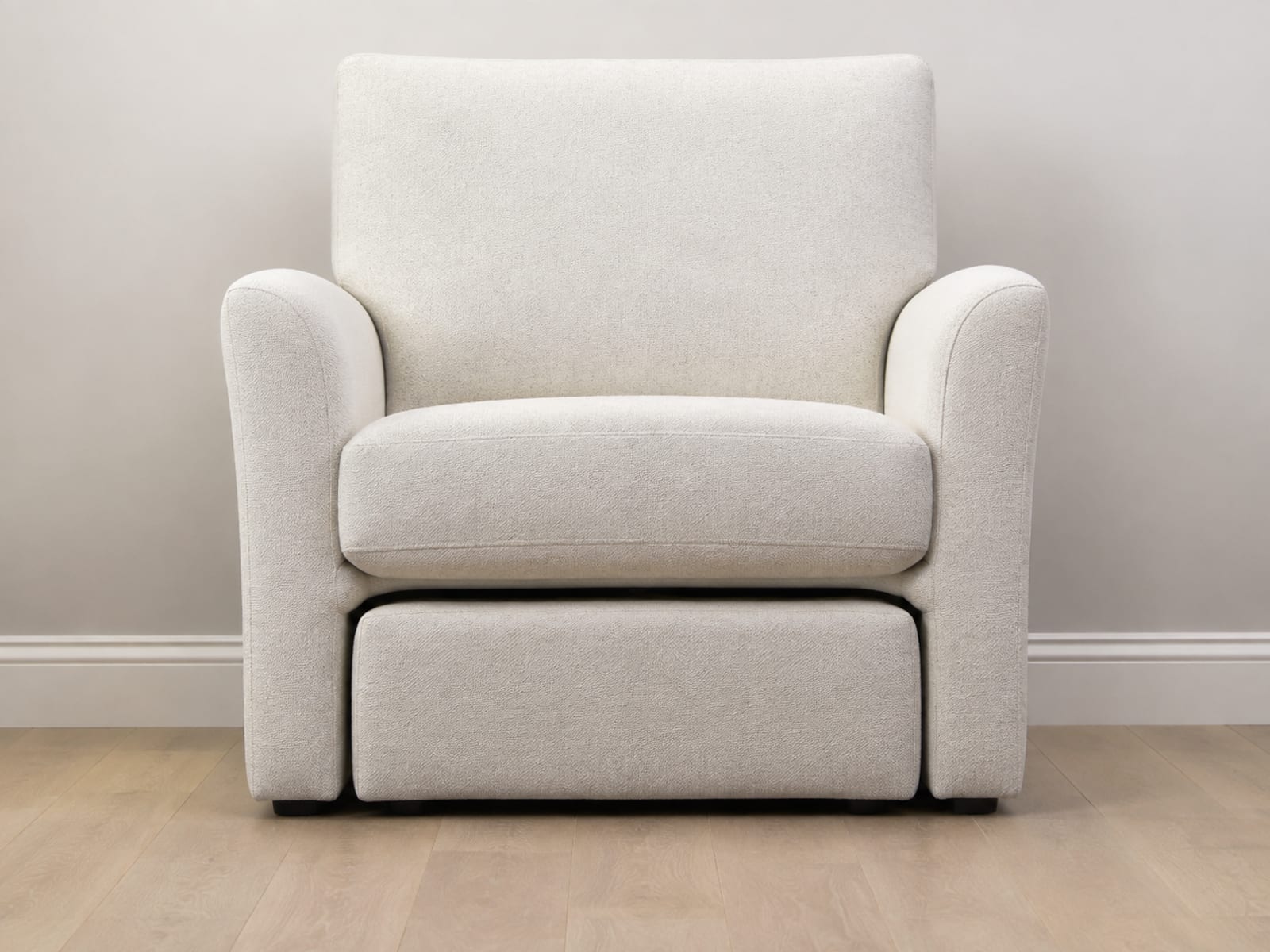 An armchair seen square from the front at low height with a matching footstool pushed fully back beneath it, only its front face showing under the front rail