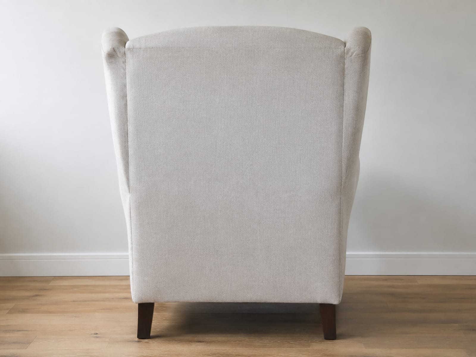 A tall winged armchair seen square from behind against a plain painted wall, the flat outside back panel and both wings curving forward at the top