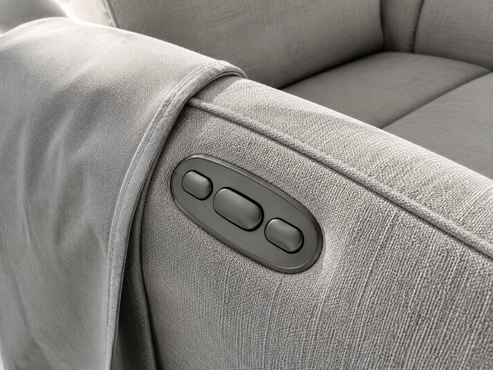 The arm of a powered recliner with its small oval control pad set into the upholstery and the edge of a fitted cover folded back clear of it
