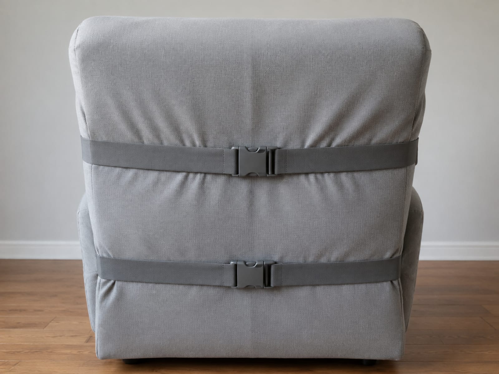 The back panel of a covered recliner seen from behind, with two elastic bands running across it and clipped together with plain buckles