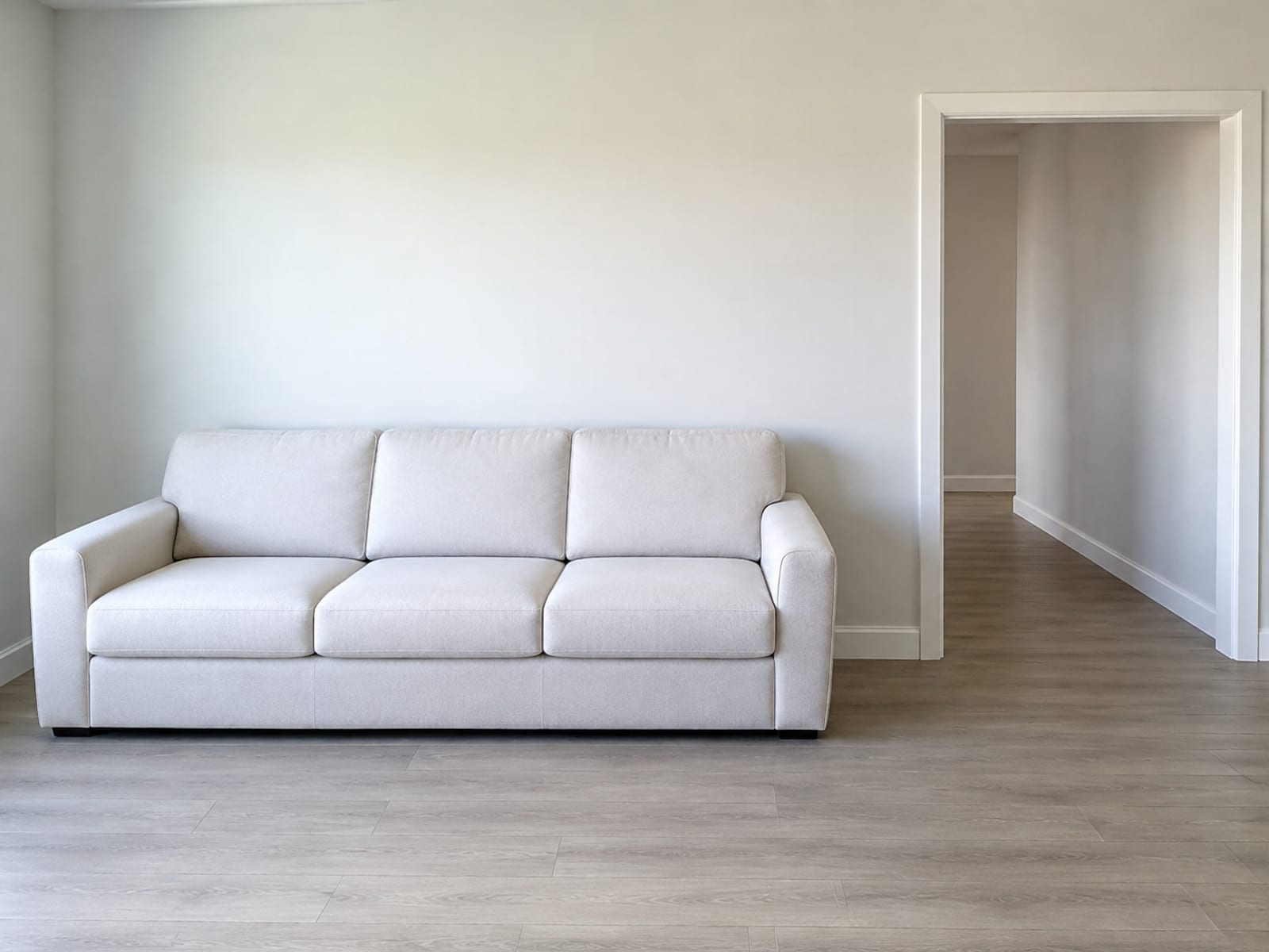 A long closed reclining sofa against one wall of a bare room with an open interior doorway in the same wall, both the sofa width and the door opening in frame