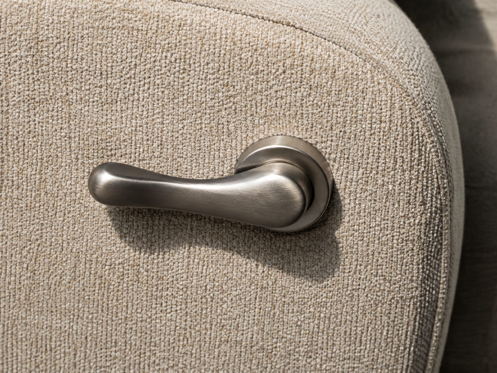 An extremely close view of a plain unmarked metal release lever mounted on the outer side of an upholstered sofa arm