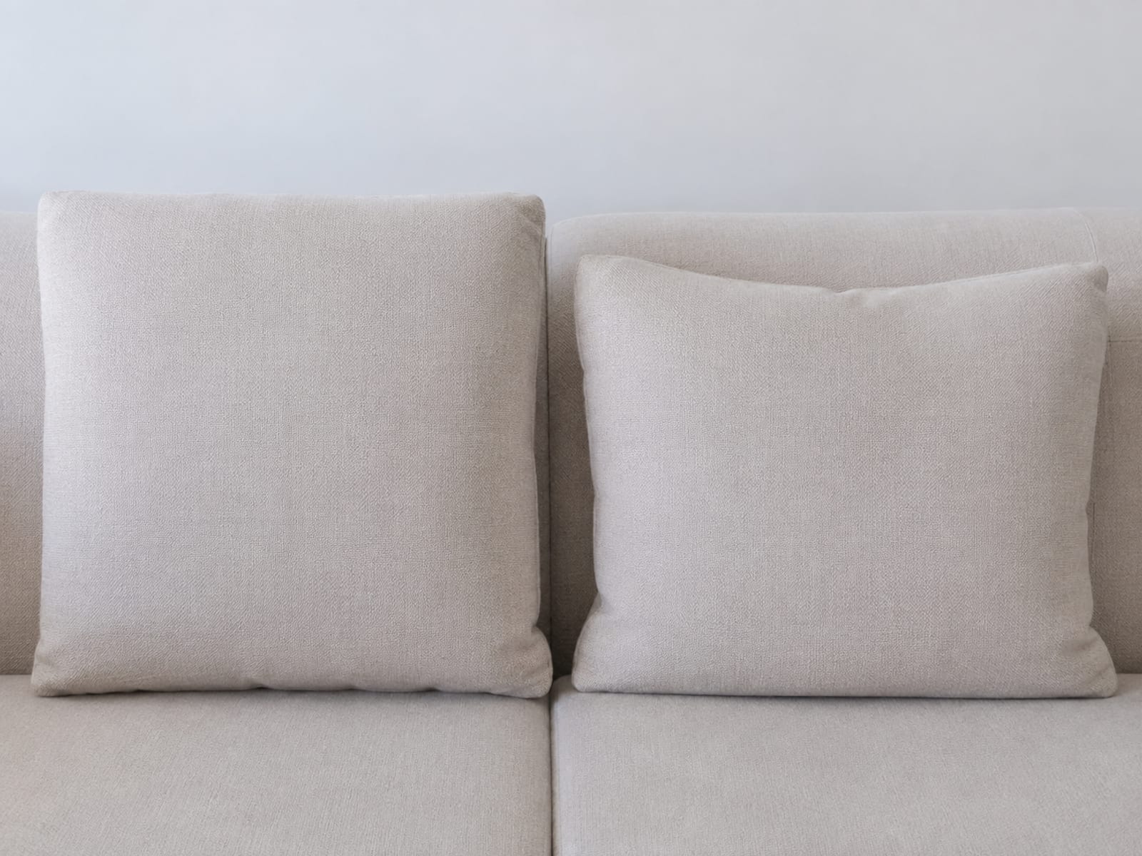 Two back cushions resting side by side, the left standing full and square and the right settled lower with a shallow dip along its top edge