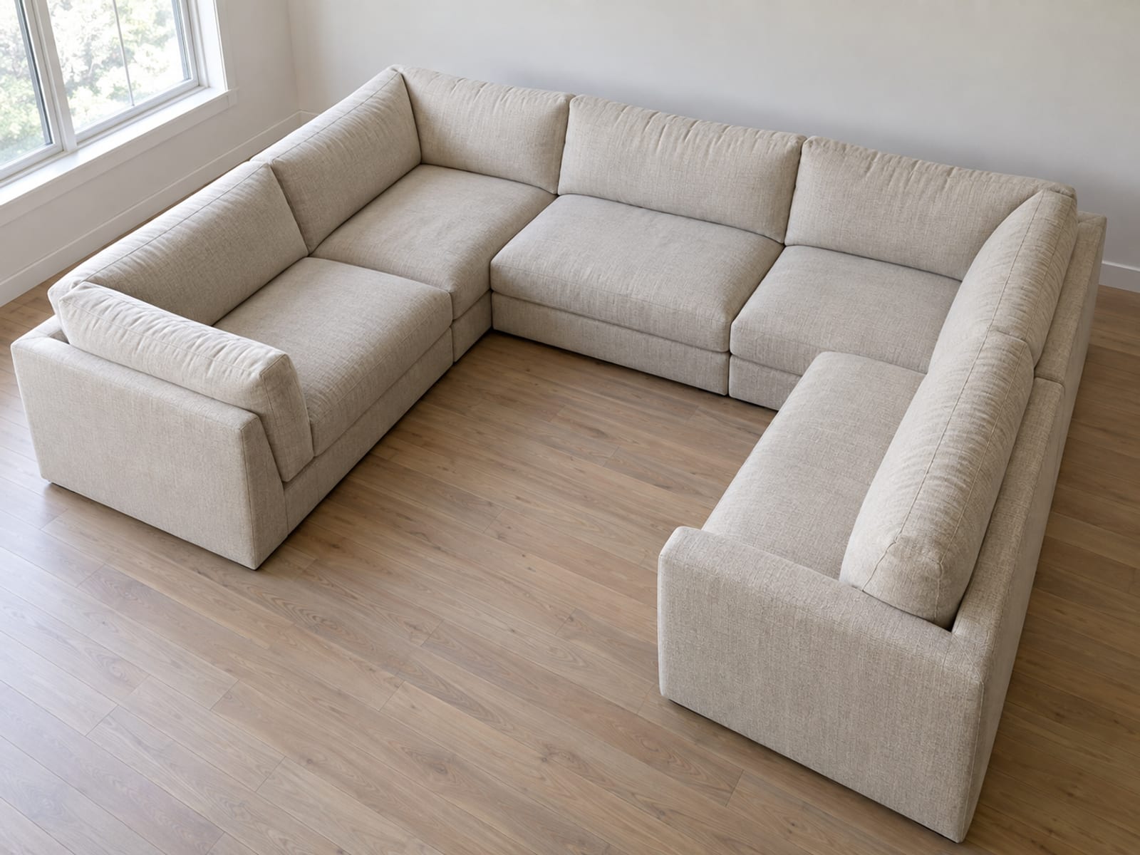 A six-seat U-shaped sectional in a plain daylit room photographed from a raised position just outside and above one back corner, looking diagonally over its back and across the enclosed seating area inside the U