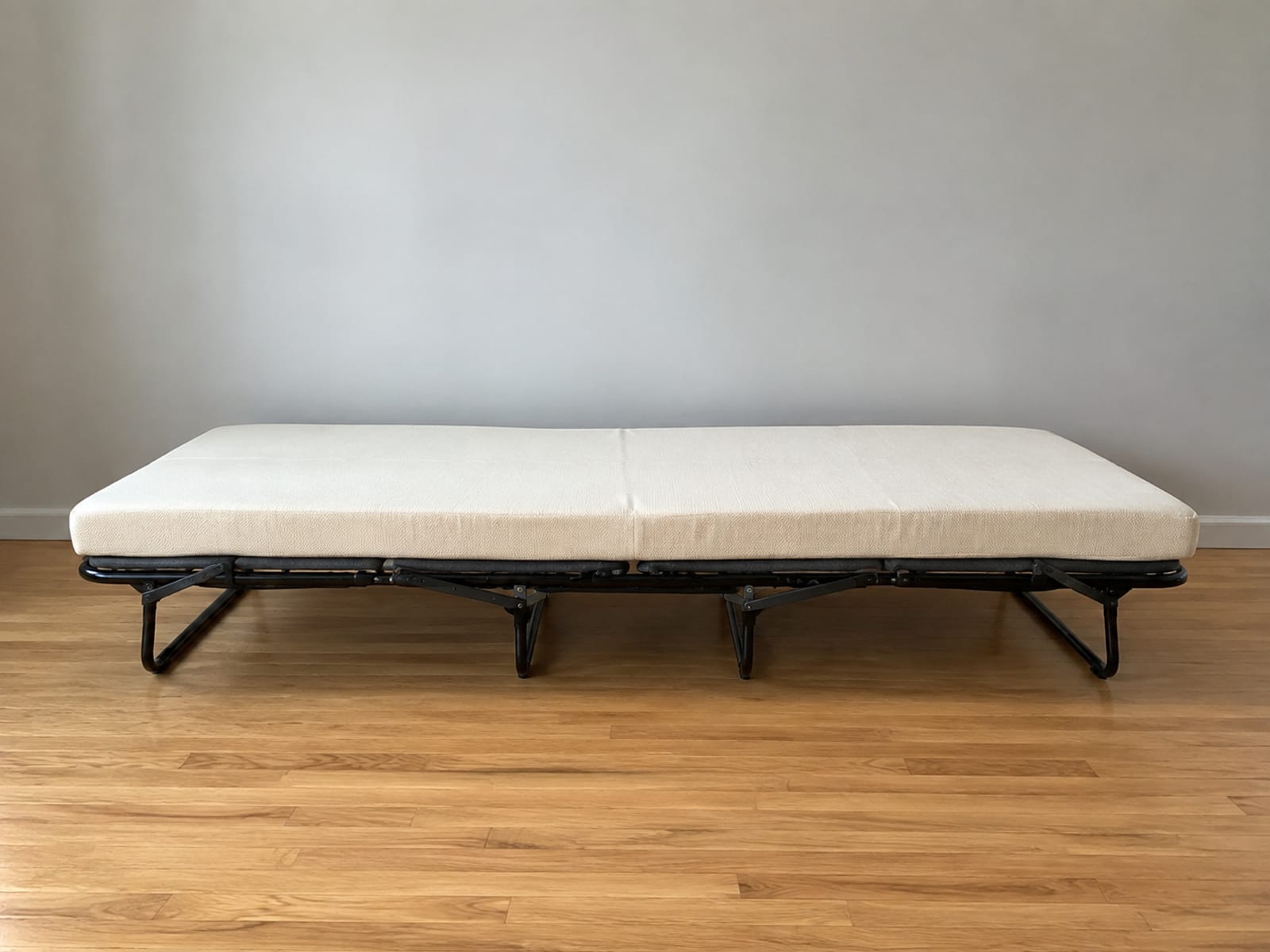 An opened sleeper chair seen square from the side at floor level, the full run of its bare sleeping surface lying as one long band across the frame