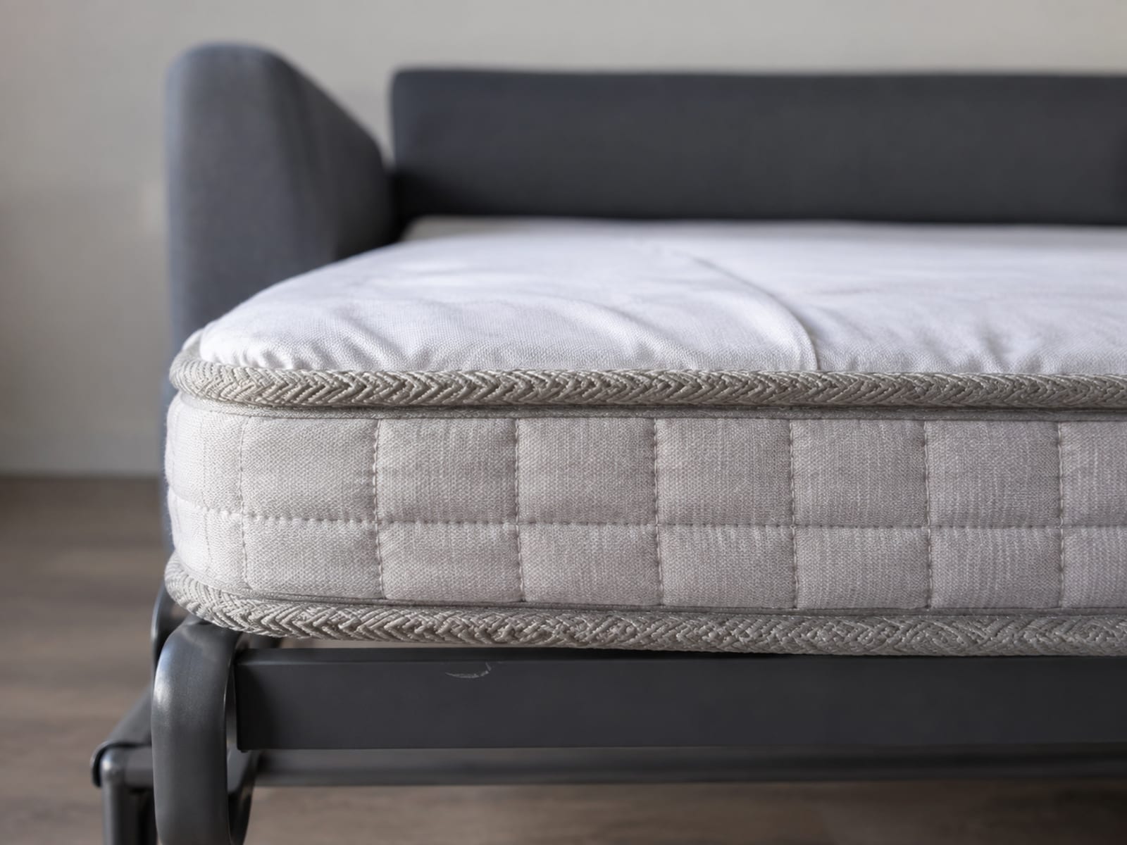 The side edge of an opened sleeper mattress on its frame, its thickness reading as a band above the metal rail below
