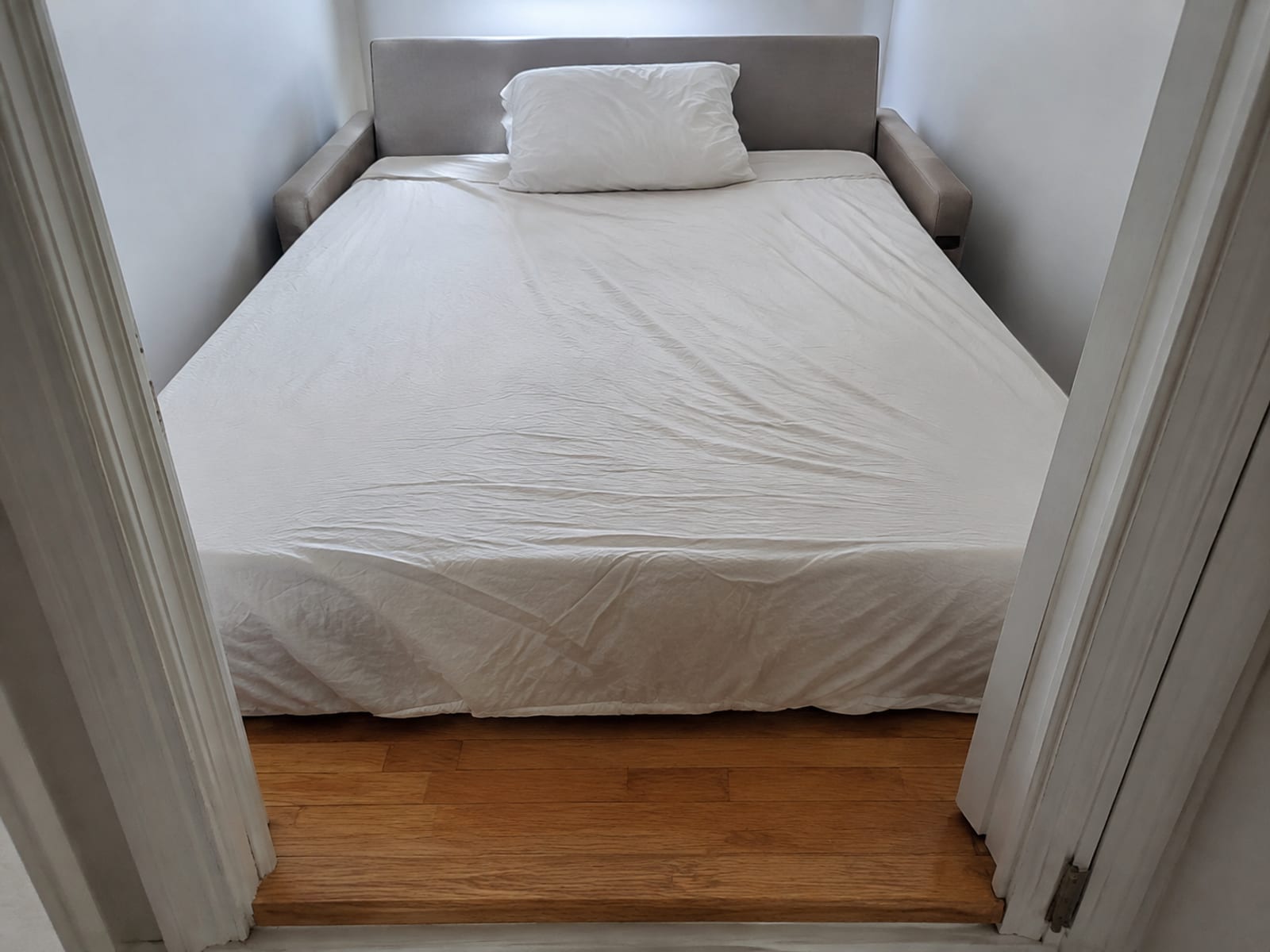 A sleeper sofa opened into its bed in a small room, with only a narrow strip of floor left between the foot of the bed and the near wall
