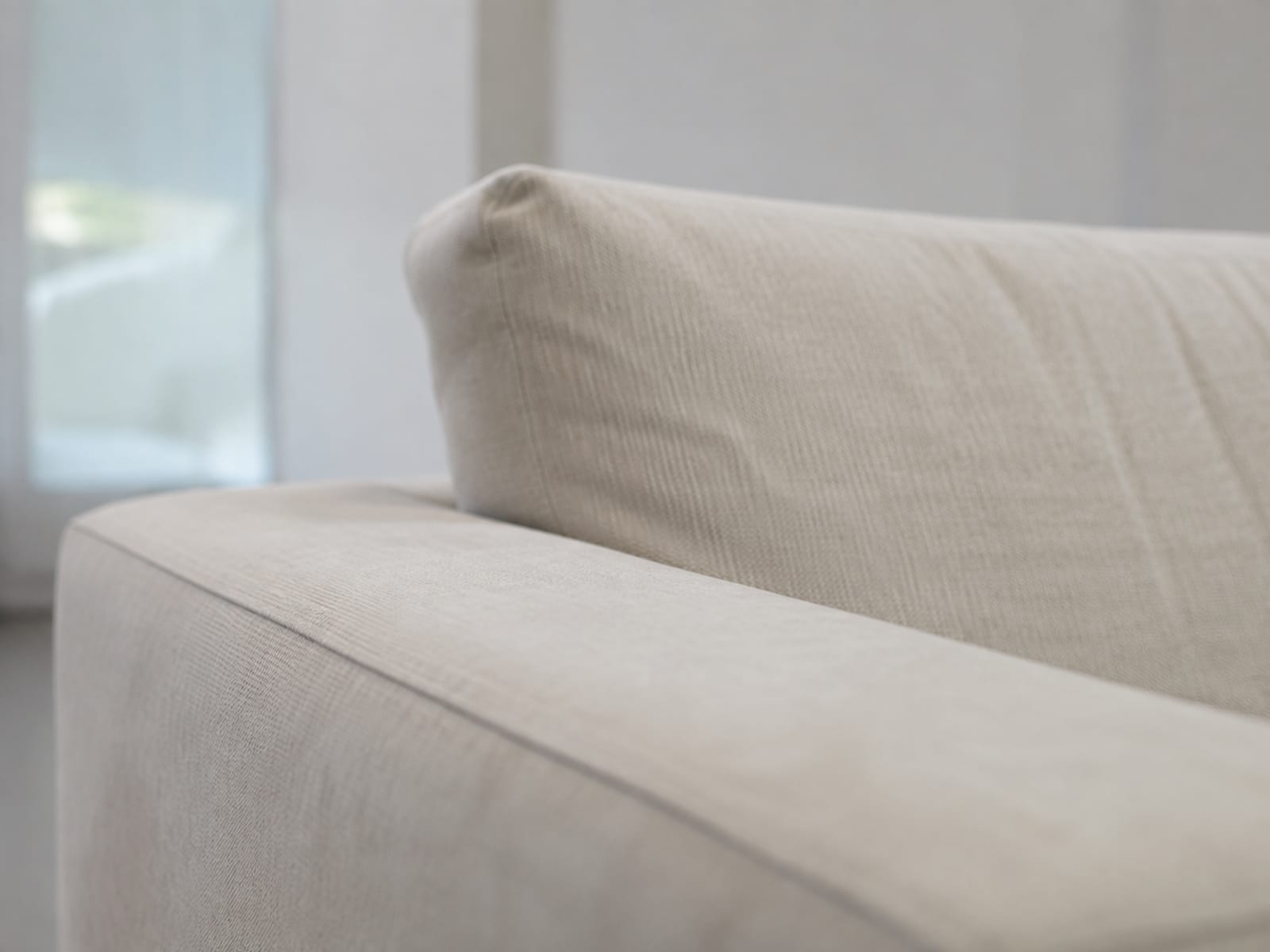 A close view along the flat top of a sofa arm running away from the camera, with the back cushion rising clearly higher behind it