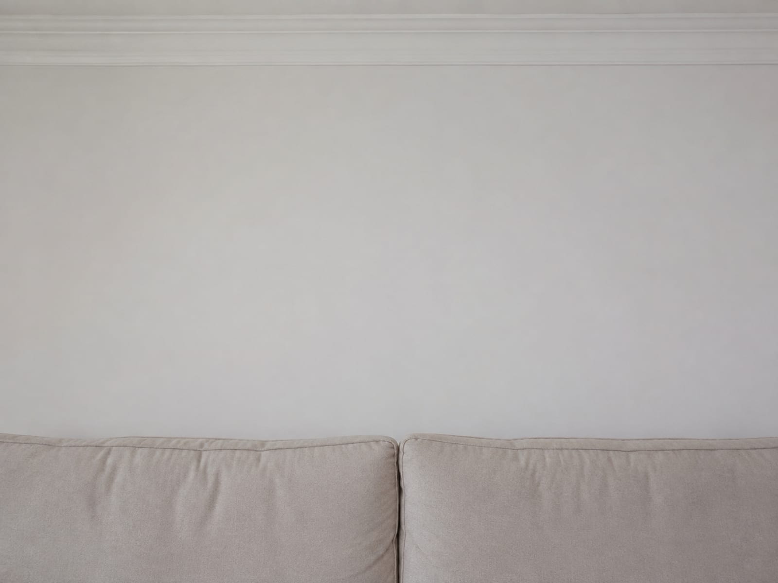 The top edge of a sofa back cushion running across the lower third of the frame with plain painted wall rising above it to a picture rail
