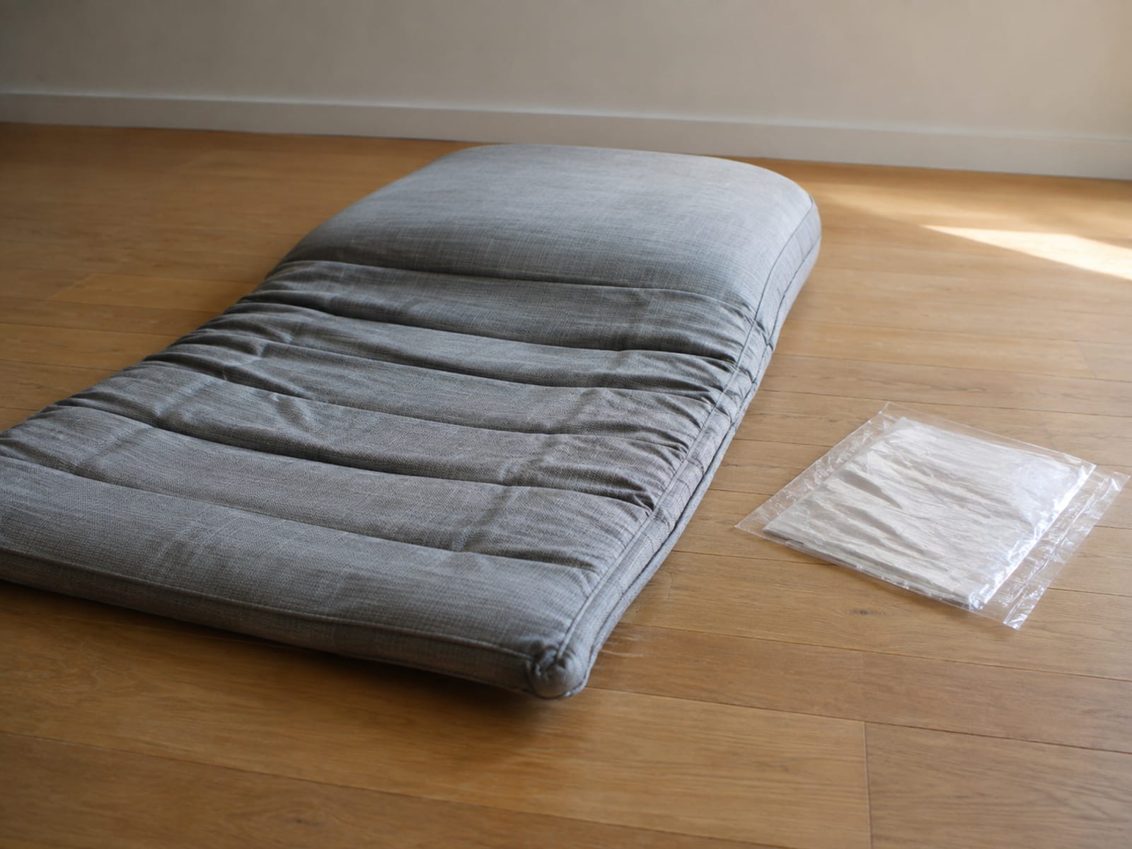 A sofa cushion half recovered from compression, one end still flat and deeply creased, the other risen to full thickness