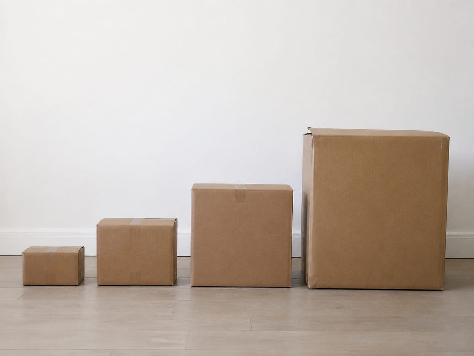 Four compressed furniture cartons of increasing size lined up left to right on a bare floor