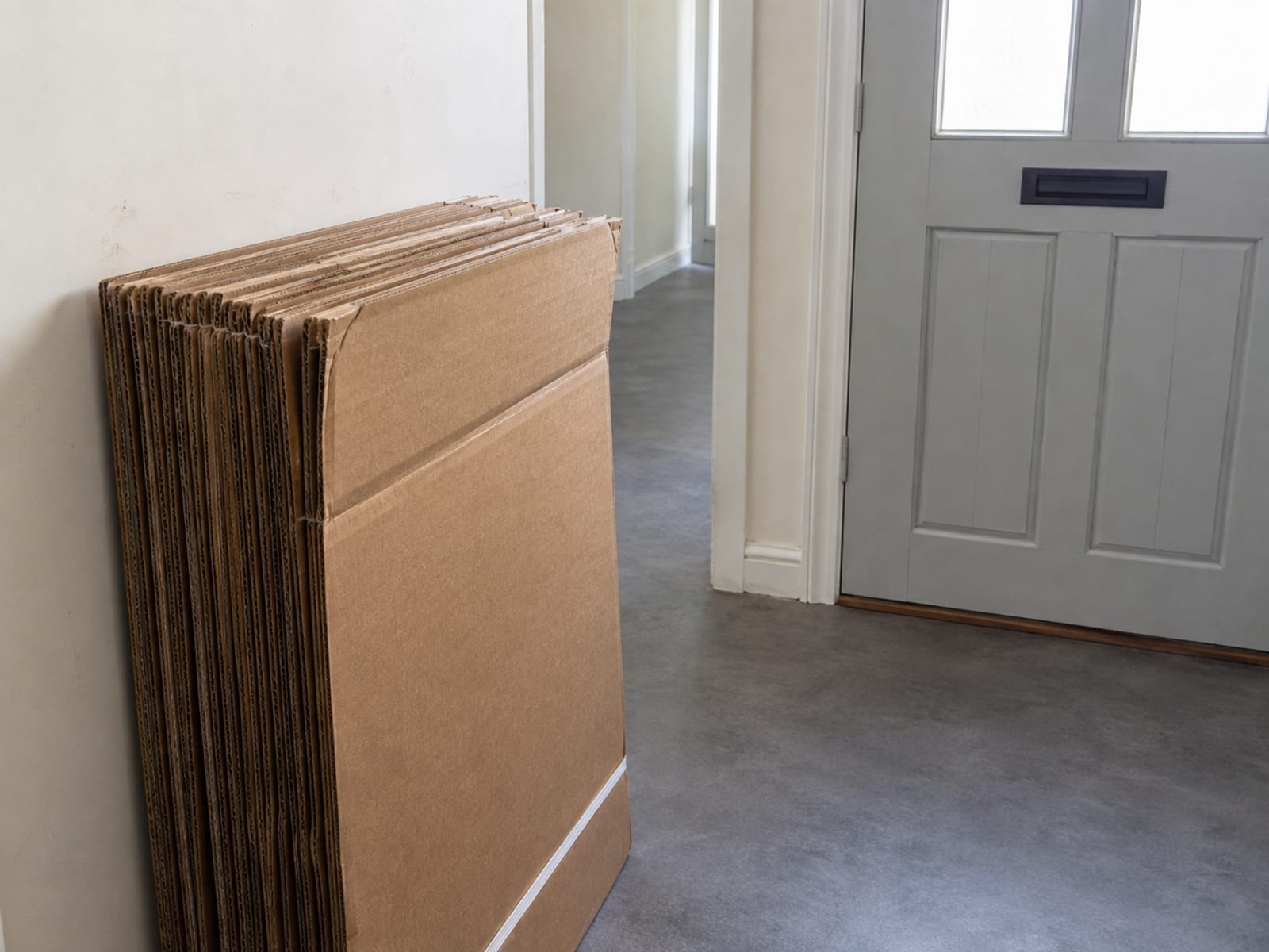 The flattened remains of several large cartons folded and stacked neatly beside a front door, ready to go out