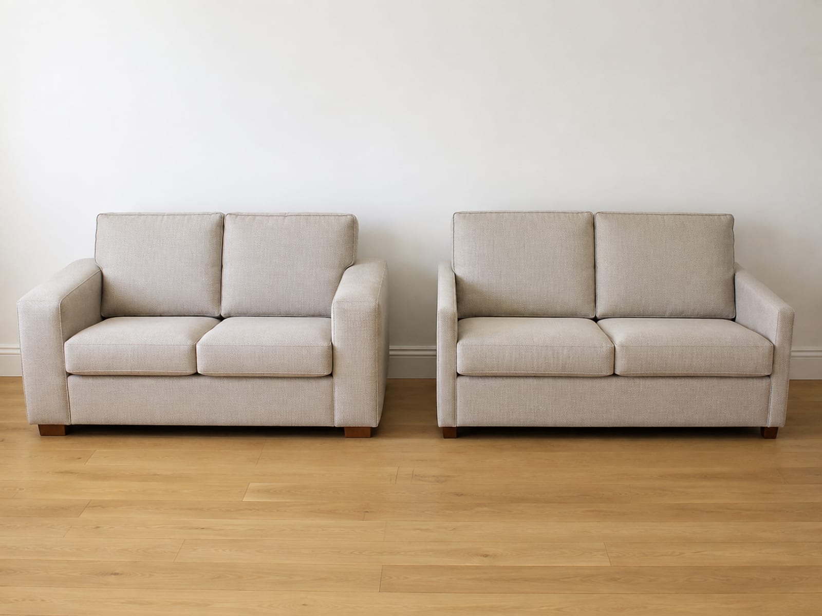 Two loveseats of the same overall width side by side, one with wide upholstered arms and one with slim arms