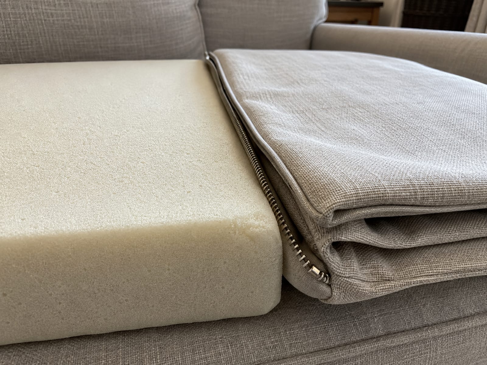 A loveseat seat cushion cover removed and folded beside the bare foam block, the open zip running along the cushion edge