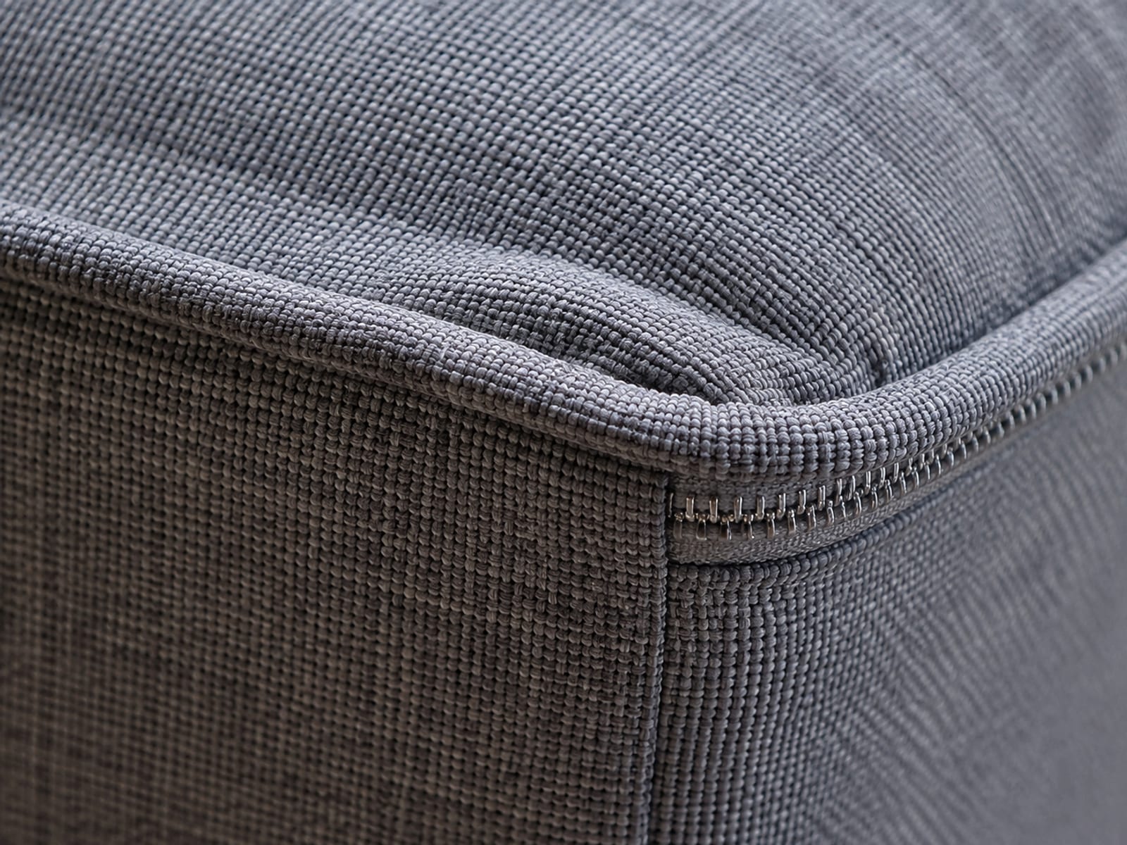 Close view of a sofa cushion corner where the woven cover, a stitched seam and a zip line meet