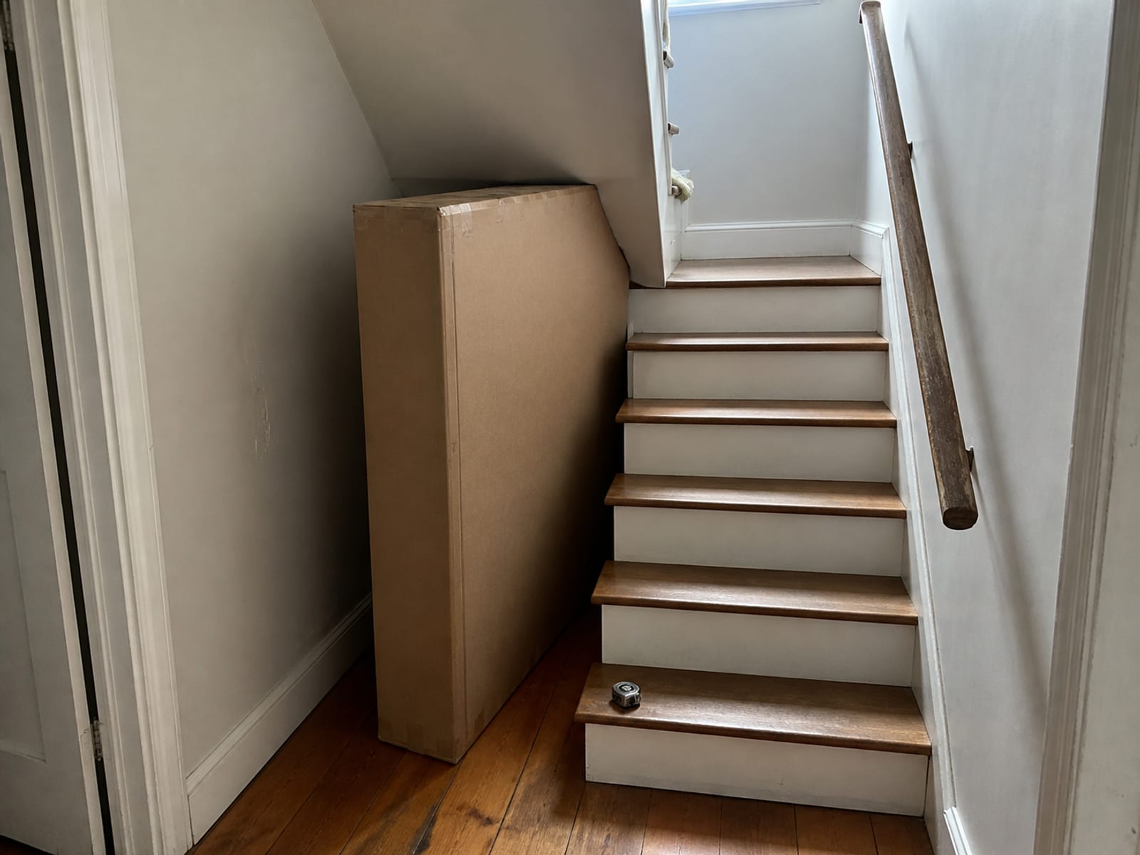 A flat sofa carton stood at the foot of a staircase that turns, with the low ceiling above the turn in frame