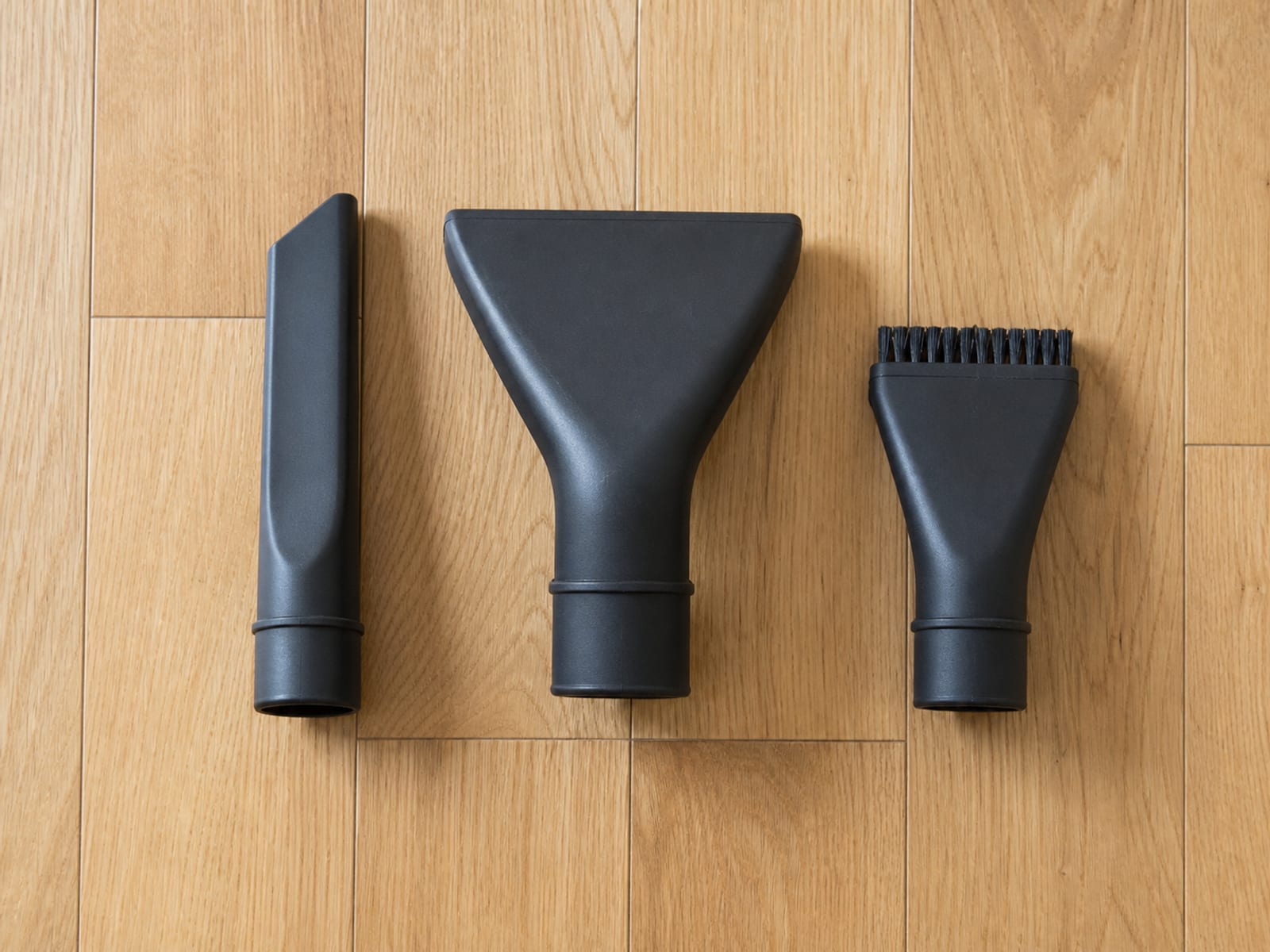 Three plain unbranded cleaning tools laid out in a row on bare floorboards, seen from above