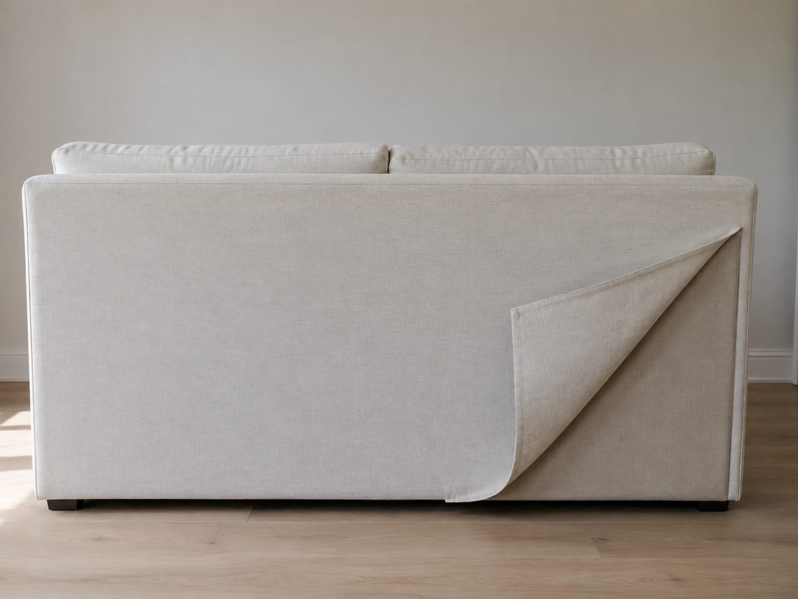 The outside back of a sofa with the bottom corner of its cover unfastened and turned up to show the plain unfinished lining beneath