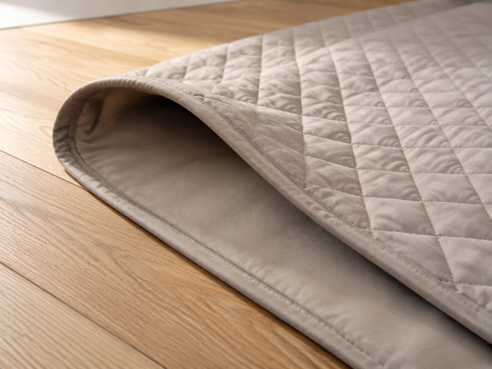 One corner of a plain cover folded back on floorboards, the smooth matte inner face showing against the quilted outer face of the same piece